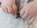 Kinderhände halten ein Schleichtier und gestalten mit dessen Hilfe dieses Bild mit Sand und Kleister.