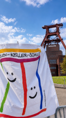 Das Bild zeigt das Logo der LVR-Helen-Keller-Schule vor dem Hintergrund des F&ouml;rderturms der Zeche Zollverein.