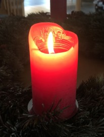 Das Bild zeigt eine brennende rote Weihnachtskerze.